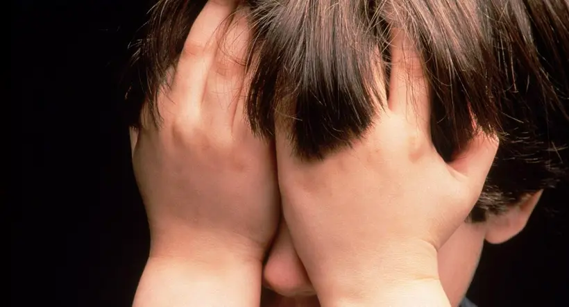 Foto ilustrativa de un niño con los ojos tapados con las manos para nota de un menos que llora a su padre en una tumba
