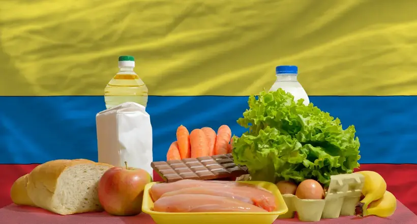 complete national flag of colombia covers whole frame, waved, crunched and very natural looking. In front plan are fundamental food ingredients for consumers, symbolizing consumerism an human needs
