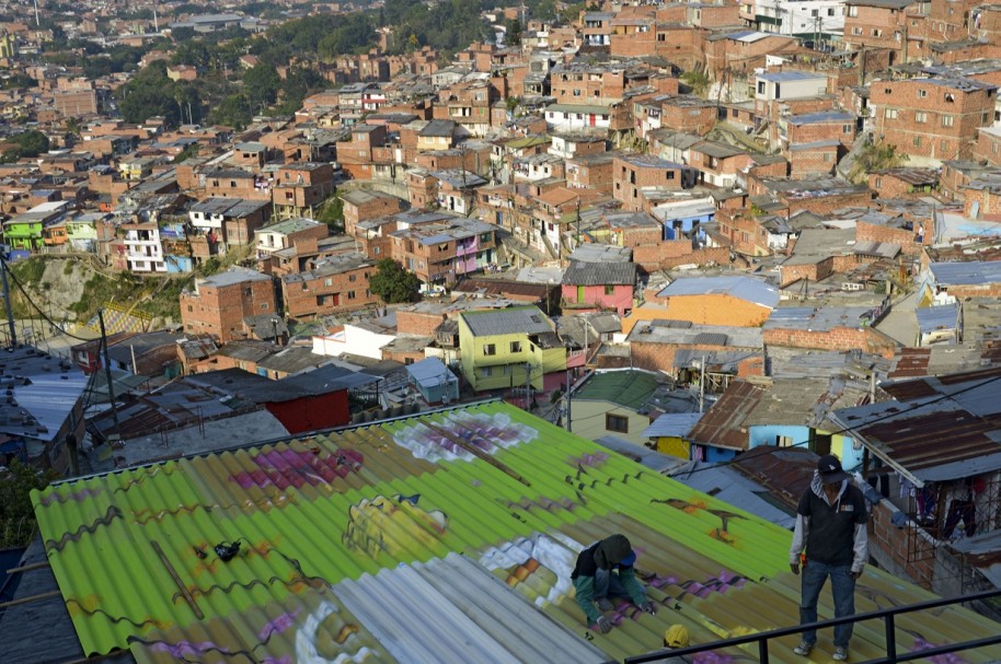 Un hombre pinta el tejado de una casa, en una comuna de Medellín