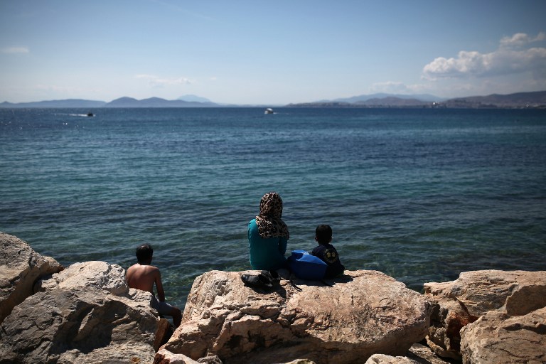 Migrants sit facing the sea near the former international airport in Athens, currently used as a temporary camp for migrants and refugees, on June 5, 2016. Problems in implementing a controversial EU-Turkey deportation deal have created a bottleneck of some 8,500 migrants on Greek islands, where brawls in overcrowded camps are common. / AFP PHOTO / ANGELOS TZORTZINIS