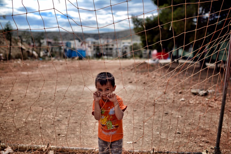 A boy looks on behind a net at the refugee camp of Schisto on June 8, 2016 in Athens. The Schisto camp, which accomodates some 1,700 migrants of all ages, the vast majority of them from Afghanistan, is an open facility where people who are assigned there are free to come and go. / AFP PHOTO / ARIS MESSINIS