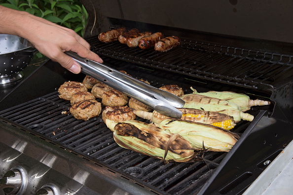 Food cooking on a gas barbecue. Sausages, turkey burgers and corn. (Photo by: Education Images/UIG via Getty Images)