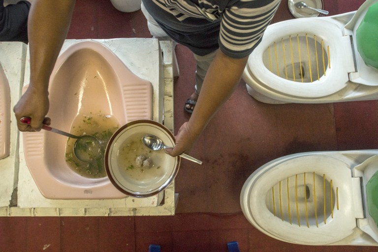 This picture taken on July 16, 2016 shows customers being served meatball soup from a squat toilet during a meal at the "Jamban Cafe" in the city of Semarang on Java island, a small eatery where a handful of diners sit on upright toilets around a table where food is served in two squat toilets. The toilet-themed cafe where customers dine on meatballs floating in soup-filled latrines may not be everyone's idea of haute cuisine, but Indonesians are flocking to become privy to the latest lavatorial trend. / AFP PHOTO / SURYO WIBOWO
