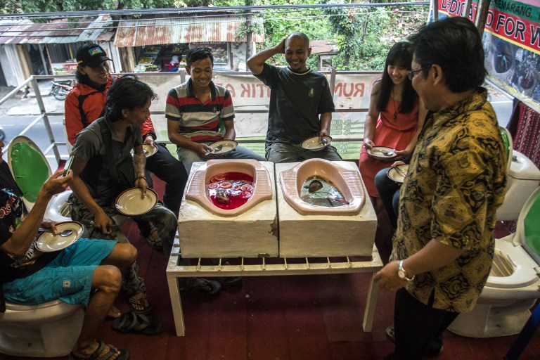 This picture taken on July 16, 2016 shows customers having a meal at the "Jamban Cafe" in the city of Semarang on Java island, a small eatery where a handful of diners sit on upright toilets around a table where food is served in two squat toilets. The toilet-themed cafe where customers dine on meatballs floating in soup-filled latrines may not be everyone's idea of haute cuisine, but Indonesians are flocking to become privy to the latest lavatorial trend. / AFP PHOTO / SURYO WIBOWO