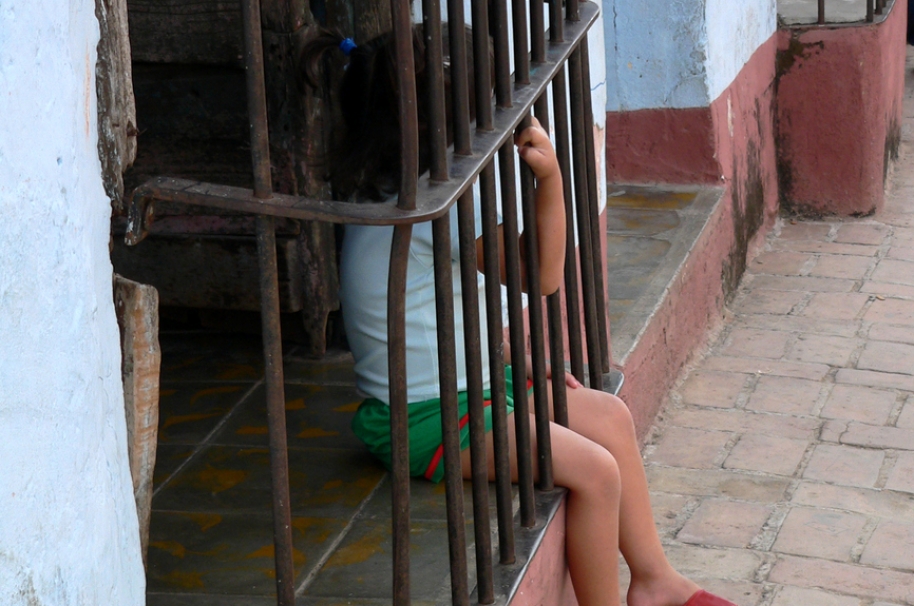Niña mirando por ventana de su casa, en Cuba. Pulzo.com