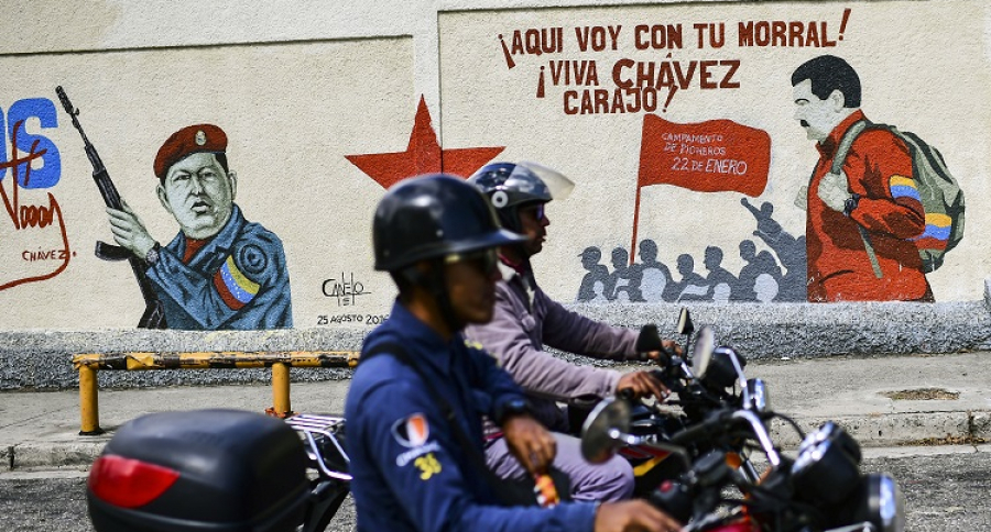 Motociclistas pasan frente a paredes pintadas con Chávez y Maduro
