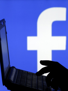 Hombre con un computador y fondo de Facebook