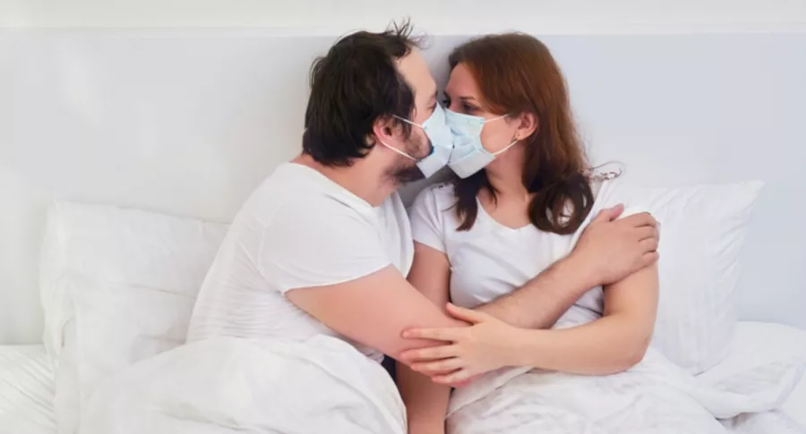 Pareja en una cama se 'besa' con tapabocas, ilustra nota de recomendación de usar mascarilla durante el sexo