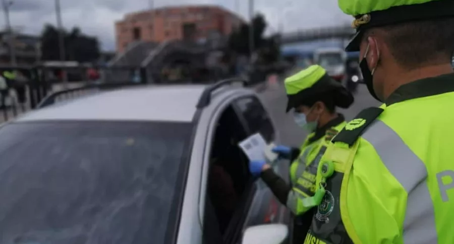 Policía revisando documentos de conductor, en Bogotá. Conozca las infracciones y las multas que pueden ponerle si incumple normas de tránsito. 