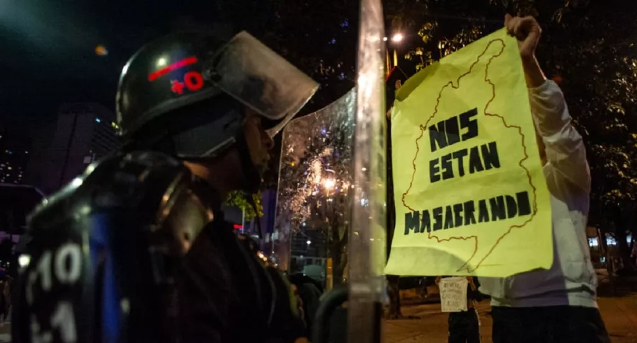 Policía frente a un manifestante que muestra un letrero de 'Nos están masacrando', durante las protestas de septiembre del 2020