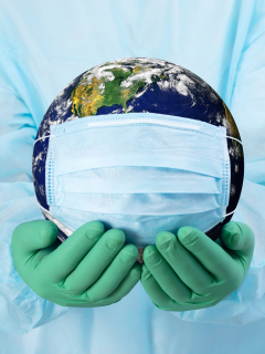 Manos de médico con guantes que sostienen el planeta Tierra con un tapabocas. Foto de referencia para ilustrar que el mundo superó el millón de muertes por COVID-19.