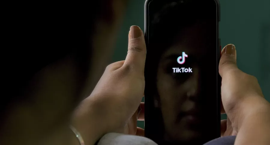 Mujer con celular u logo de aplicación TikTok ilustra artículo TikTok seguirá operando en EE.UU. temporalmente.