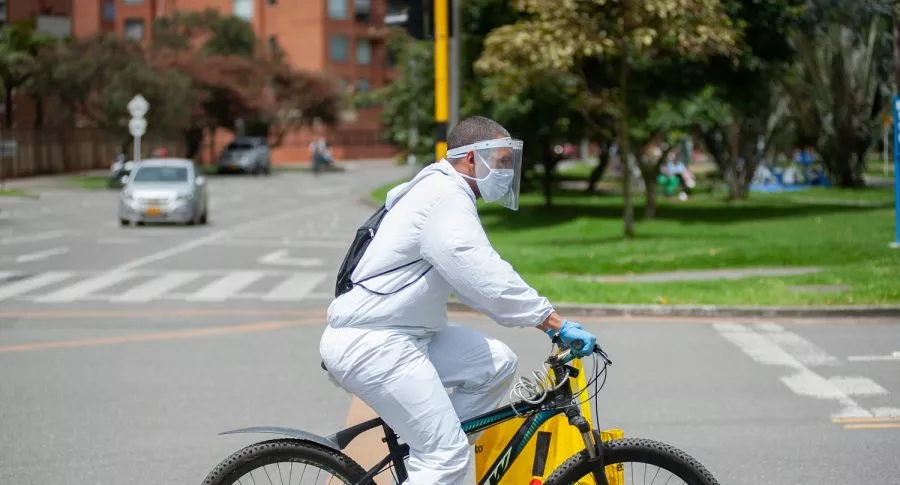 Imagen de hombre en bicicleta con traje de bioseguridad ilustra nota de posibilidad de volver a cuarentena en Colombia, por rebrote.