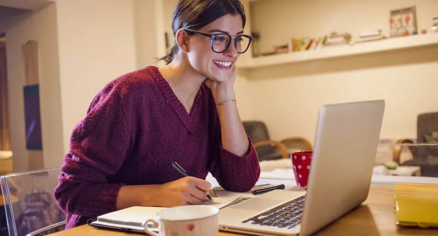 Imagen de mujer sonriendo mientras ve su computador para ilustrar nota sobre qué foto se debe usar en LinkedIn para buscar empleo