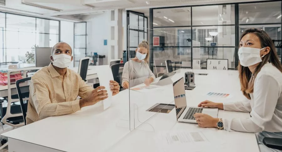 Personas trabajando en oficina con tapabocas y separadas por un vidrio para ilustrar nota sobre los modelos de oficina del futuro
