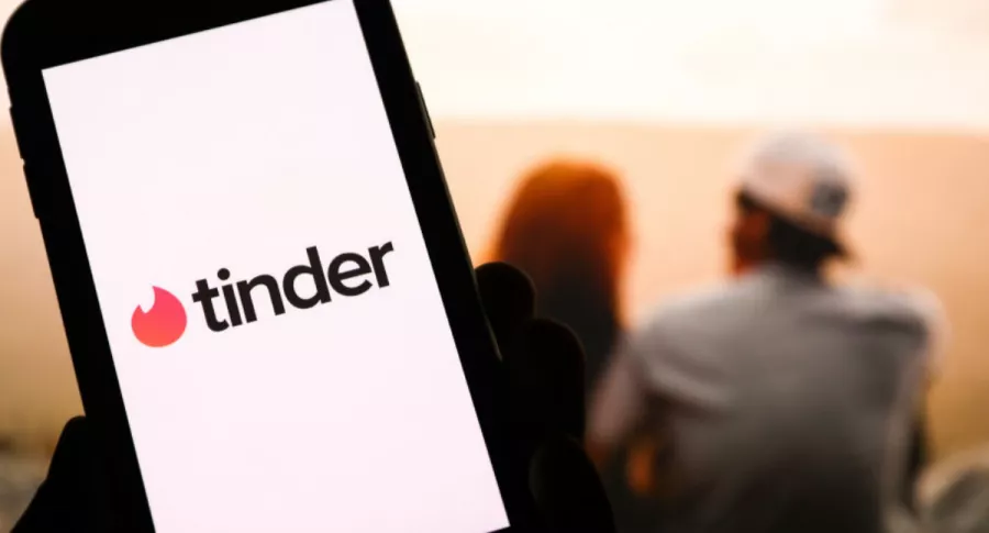 Logo de Tinder en un celular con una pareja de fondo.