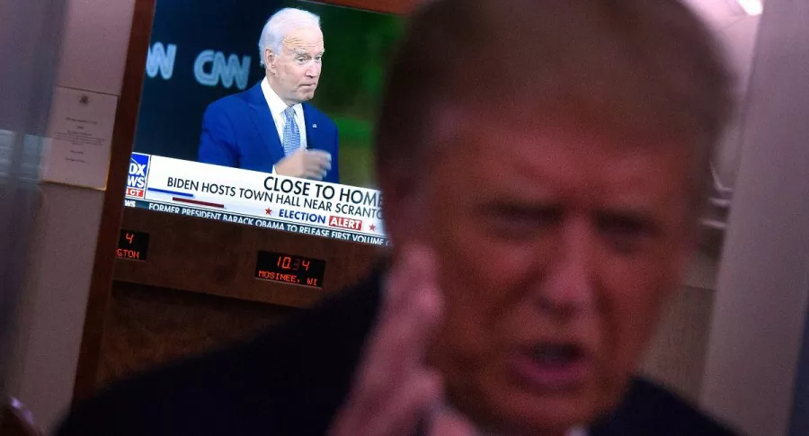 Donald Trump aparece con un televisor detrás en el que está Joe Biden, en medio de las campañas de las elecciones en EE.UU.