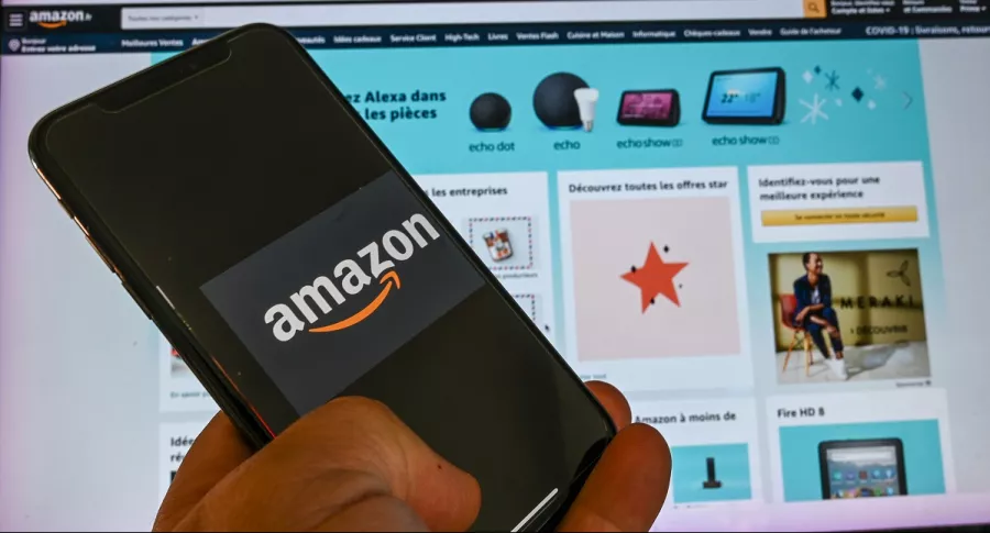 Imagen de persona que posa con un celular que muestra el logotipo de Amazon, frente a una pantalla de computador, ilustra artículo Farmacia digital de Amazon hace temer fin de droguerías.