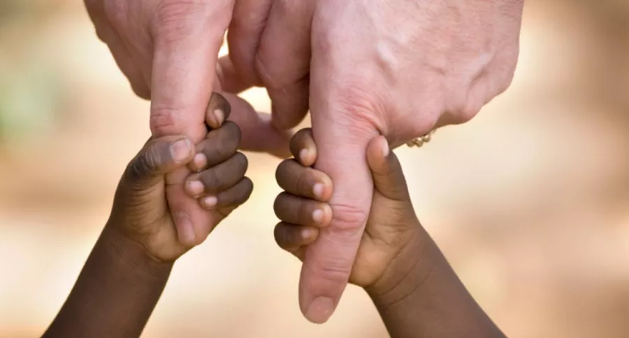Niños afro toman de la mano a pareja blanca, ilustra nota de pareja se arrepiente de adoptar hermanos y los dejan en policía