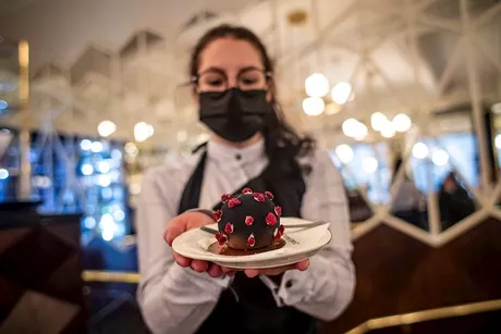 Una mesera posa mientras sostiene un pastel con forma del coronavirus durante la reapertura en el café Cerna Madona en Praga / EFE. 