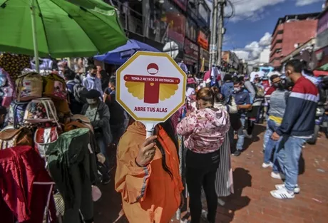 Un trabajador del Distrito sostiene un cartel que dice: “Toma 2 metros de distancia. Abre tus alas”, mientras la gente compra. ¿Será suficiente? / AFP. 