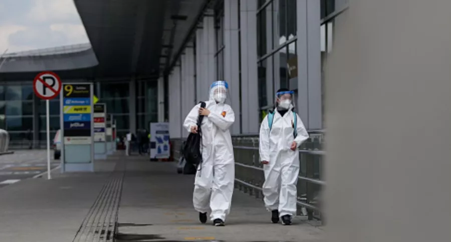 Personas con traje antifluidos en aeropuerto El Doradoilustra nota de nuevos casos de coronavirus en Colombia, para el primero de enero de 2021