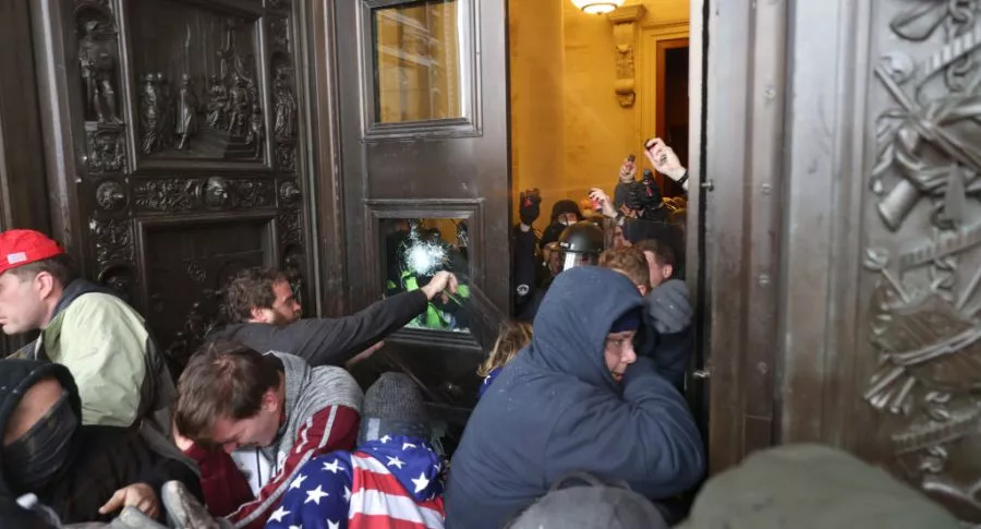 Asaltantes del Capitolio de Washiington en una de las puertas, ilustra nota de policía que se toma fotos con manifestantes violentos