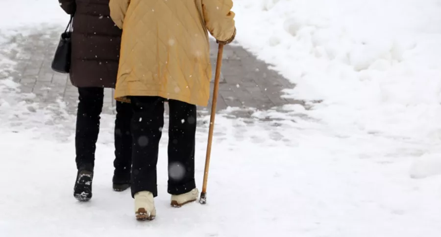 Anciana camina con bastón sobre la nieve con compañía, ilustra nota de Anciana camina 10 km bajo la nieve para recibir vacuna contra el coronavirus 