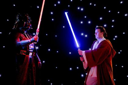 Lord Vader y un jedi chocan sables de luz, en la eterna pelea del lado oscuro y el lado luminoso de Star Wars, de Disney.