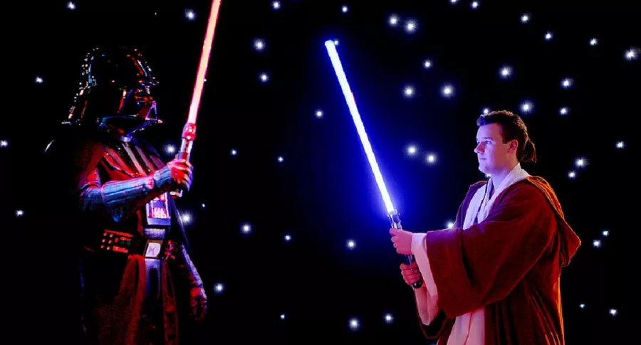 Lord Vader y un jedi chocan sables de luz, en la eterna pelea del lado oscuro y el lado luminoso de Star Wars, de Disney.