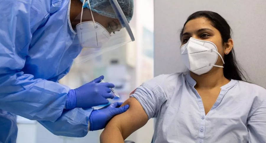 Mujer con equipo de protección completo realizando vacunación contra coronavirus en paciente. Ilustra nota sobre los 1.000 millones de vacunas aplicadas en el mundo contra la COVID-19.