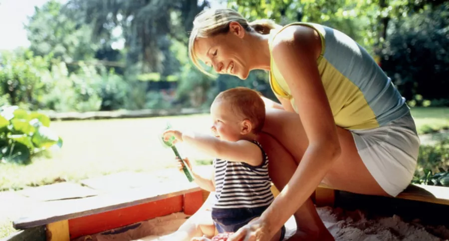 Mujer con su hijo en arenera, ilustra nota de videos de mamá vegana deja que su bebé mastique y lama arena, piedras y más