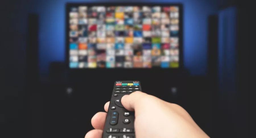 Foto de persona con control de televisión y televisor, en nota de Netflix y si necesita publicidad o subir precio, según analista.
