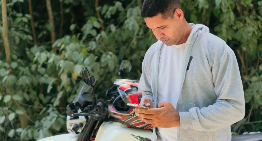 Foto de persona con moto viendo celular, en nota de dónde pagar el impuesto de la moto.