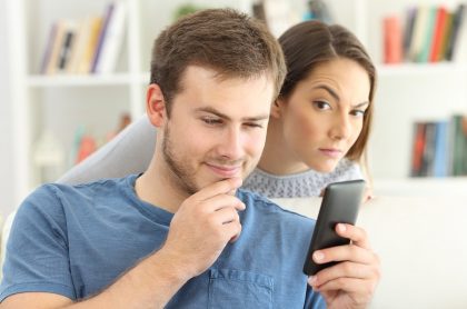 Mujer espía a su pareja mientras ve el celular, ilustra test para saber si estás en un relación tóxica.