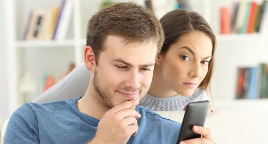 Mujer espía a su pareja mientras ve el celular, ilustra test para saber si estás en un relación tóxica.