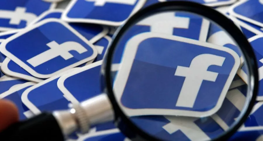Lupa sobre logos de Facebook, ilustran nota de Facebook ralentiza trabajo en nuevos productos, ante mala reputación por caída