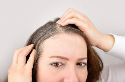 Mujer mirándose las canas ilustra nota sobre por qué salen y cómo evitarlas