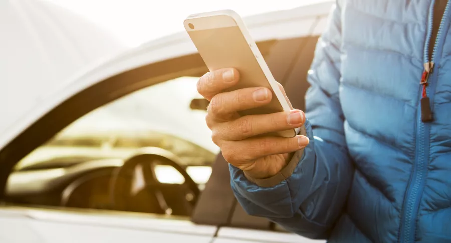 Una persona con un celular recostada en un carro ilustra nota sobre carros que se podrían comprar con lo que cuesta un iPhone 13