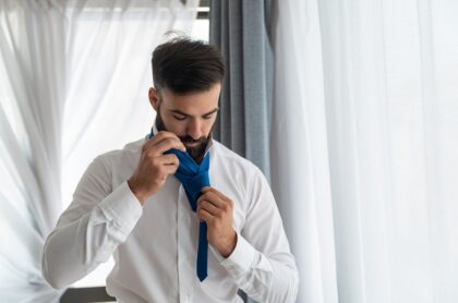 Hombre haciendo nudo de corbata, a propósito de explicación de expertos de cómo hacer el nudo sencillo y el nudo doble.