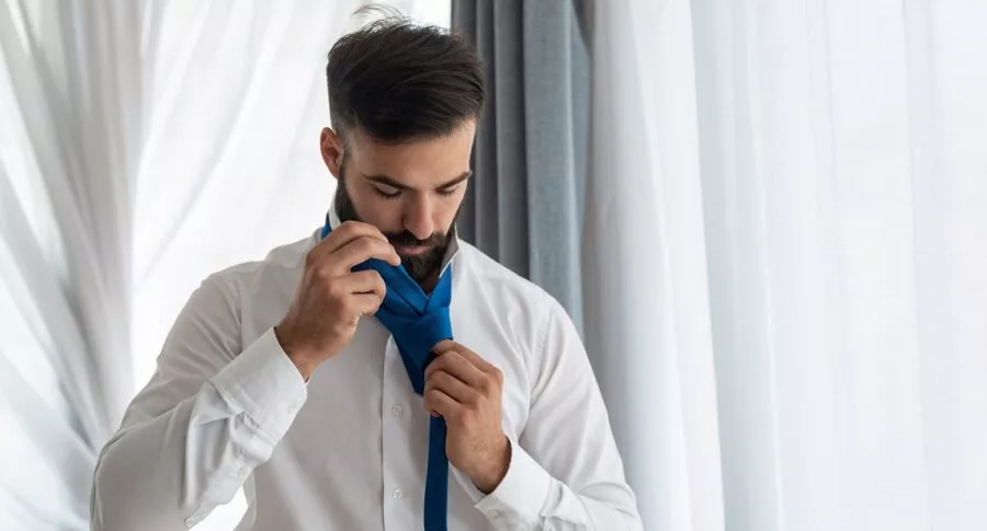Hombre haciendo nudo de corbata, a propósito de explicación de expertos de cómo hacer el nudo sencillo y el nudo doble.