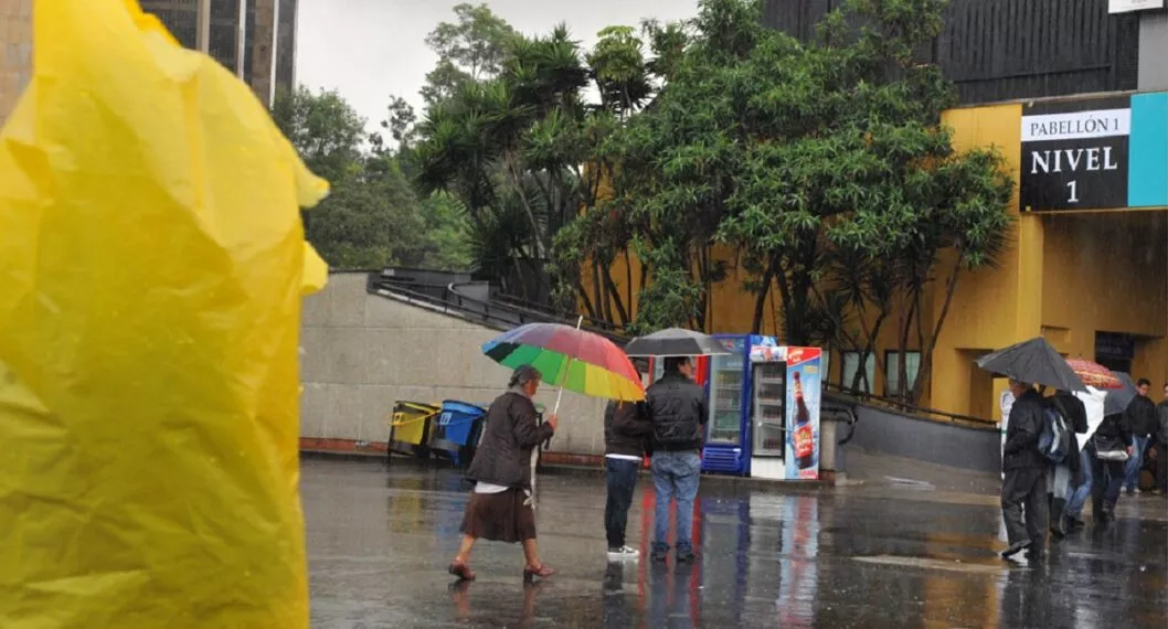 Personas con capas y sombrillas en Corferias, a propósito de que el Ideam explicó por qué está lloviendo tanto en Bogotá y en qué zona lloverá más esta semana.