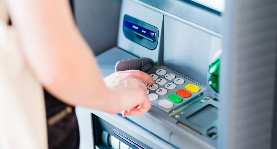 Persona en cajero automático ilustra nota sobre cómo sacar dinero sin tarjeta en Bancolombia, Davivienda, Banco de Bogotá y más