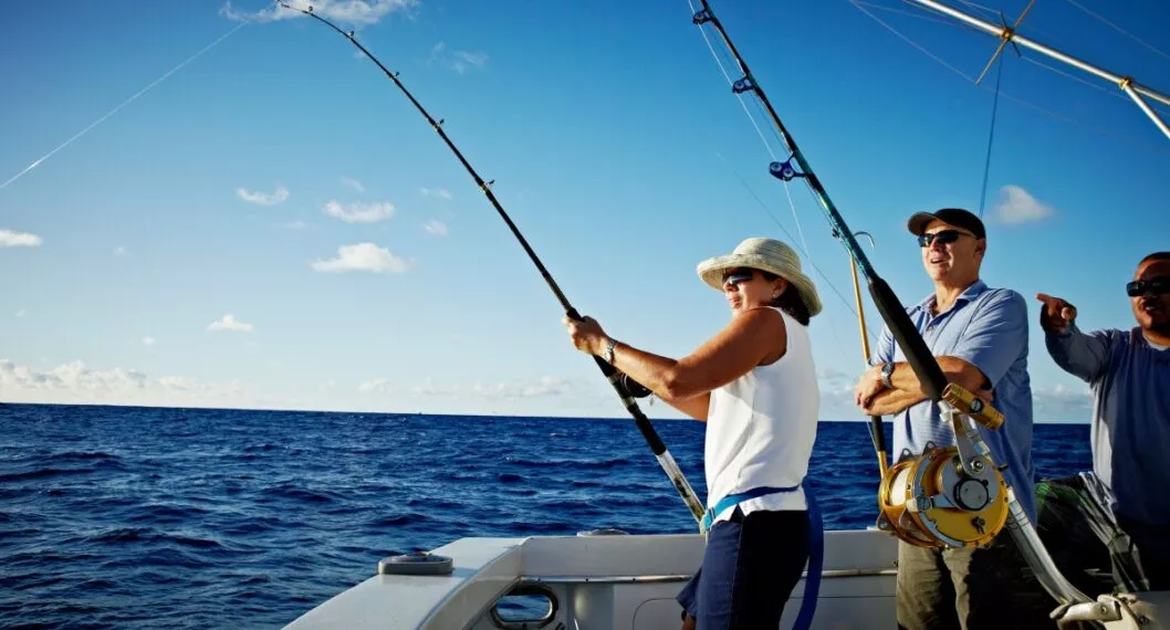 Mature woman reeling in fish husband and guide looking out at fish being reeled in