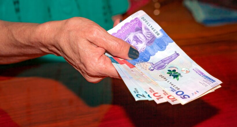 The latest Colombian currency notes in the hand of a senior latin american lady. She is showing the money before she actually makes her payment. Image shot indoors with close-up of just hands and money.