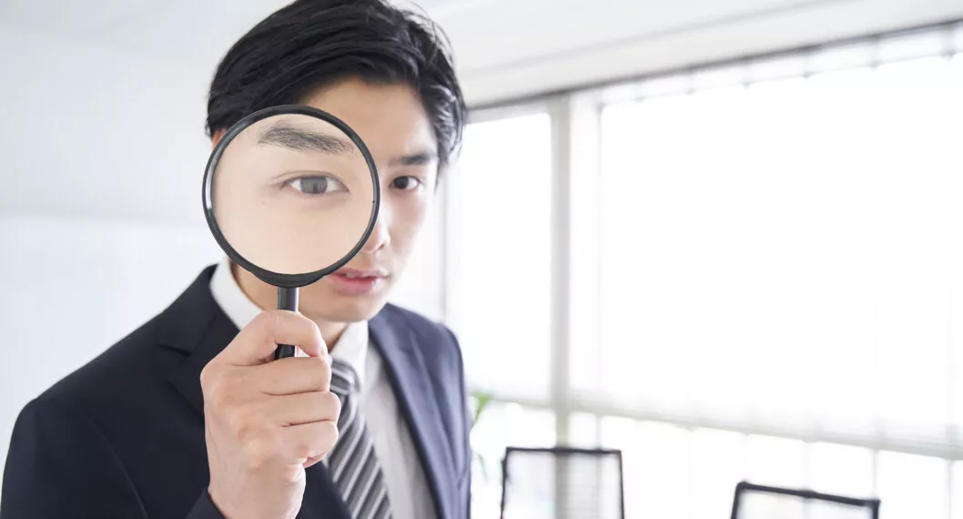 A Japanese male businessman looking through a magnifying glass in a conference room