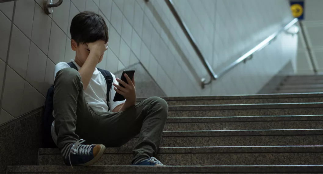 Social issues in internet technology and social media in teenager mental health. Low self esteem young Asian teenager boy sitting alone crying with smartphone, feeling frustration, fear, pain, anxiety, abused as victim of cyberbullying.