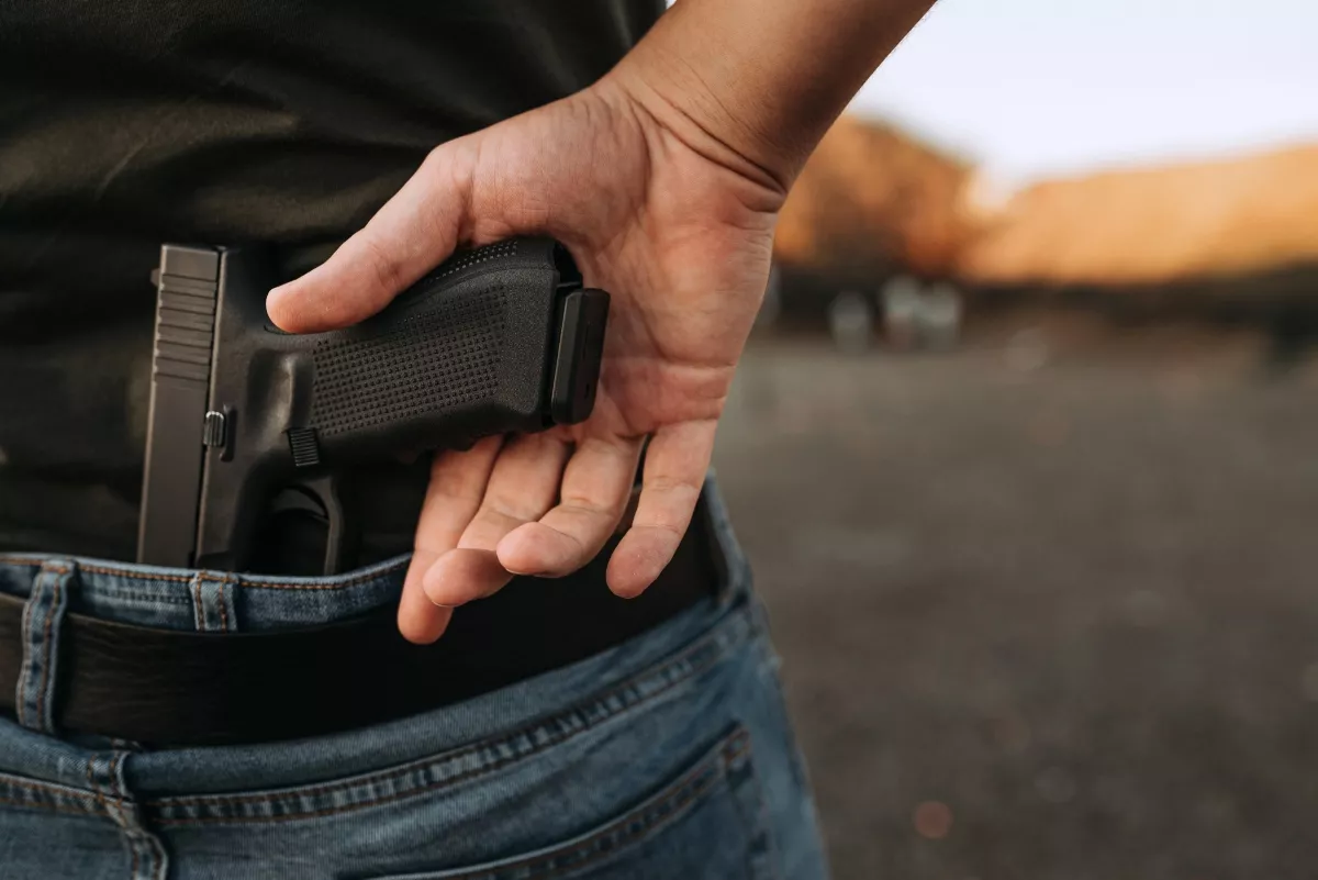 Man conceals a gun in the back of his pants, outdoors.