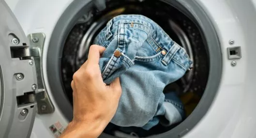 Persona colocando 'jeans' en la lavadora ilustra nota sobre cada cuánto lavarlos y cómo hacerlo para no dañarlos