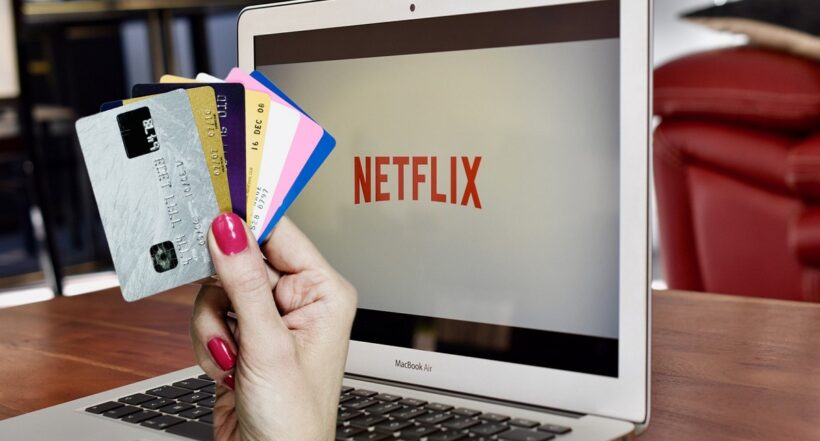 Mano de mujer sosteniendo tarjetas de crédito y Netflix en computador, en nota sobre cómo pagar la 'app' sin ese plástico